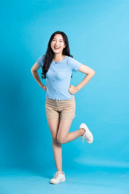 Mavi arka planda poz veren güzel Asyalı kızın tüm vücudu.
