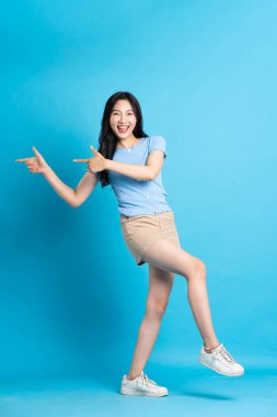 Mavi arka planda poz veren güzel Asyalı kızın tüm vücudu.