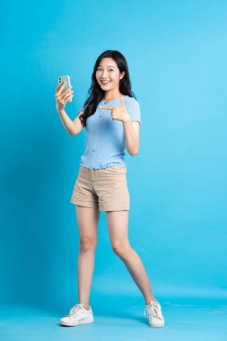 Mavi arka planda poz veren güzel Asyalı kızın tüm vücudu.