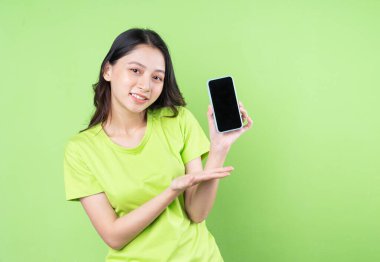 Yeşil arka planda akıllı telefon tutan Asyalı genç bir kadın resmi