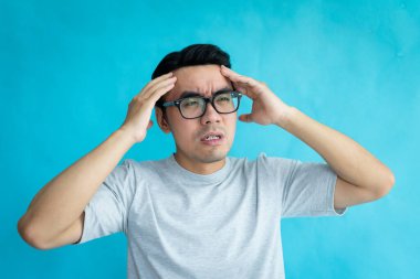 Baş ağrısı olan bir adamın portresi, mavi arka planda izole edilmiş.