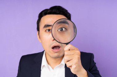 Takım elbiseli bir işadamı büyüteç takıyor, mor arka planda izole edilmiş.