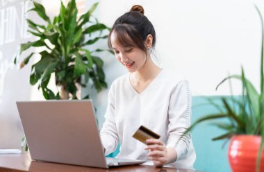 Banka kartı ve laptop kullanan Asyalı güzel bir kadının portresi.