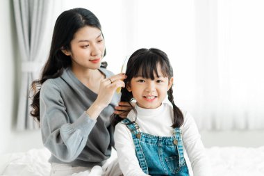 Kızının saçını tarayan bir annenin resmi.