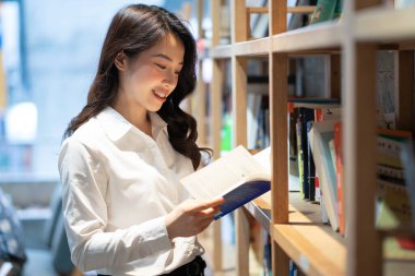 Asyalı iş kadınının kütüphanede kitap okuduğu resim