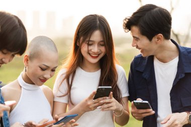 Bir grup Asyalı gencin birlikte gülüp telefonlarını kullanması.
