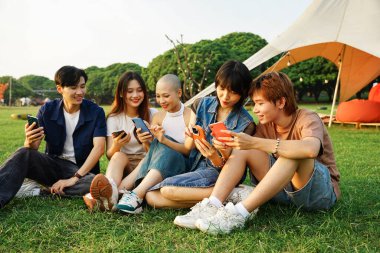 Bir grup Asyalı gencin birlikte gülüp telefonlarını kullanması.