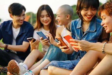 Bir grup Asyalı gencin birlikte gülüp telefonlarını kullanması.