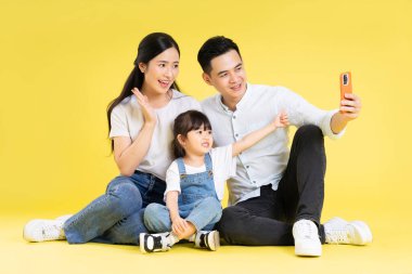 Asyalı bir ailenin sarı arka planda mutlu ve izole bir şekilde oturduğu görüntüsü