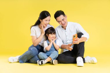 Asyalı bir ailenin sarı arka planda mutlu ve izole bir şekilde oturduğu görüntüsü