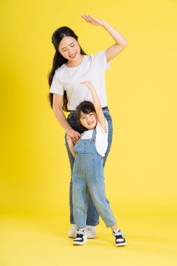 Asyalı anne ve kızının sarı arka planda poz verişi.