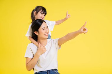 Asyalı anne ve kızının sarı arka planda poz verişi.