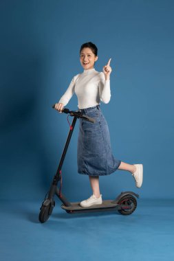 Mavi arka planda scooter süren Asyalı bir kız resmi