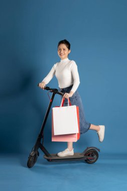 Mavi arka planda scooter süren Asyalı bir kız resmi