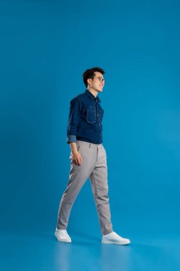 Mavi arka planda poz veren Asyalı genç iş adamının portresi
