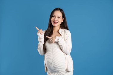 Mavi arka planda izole edilmiş hamile Asyalı kadın portresi.