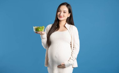 Mavi arka planda izole edilmiş hamile Asyalı kadın portresi.