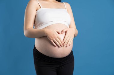 Mavi arka planda izole edilmiş hamile Asyalı kadın portresi.