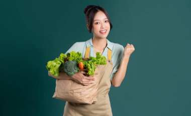 Yeşil arka planda sebze dolu bir çanta taşıyan Asyalı kız portresi.