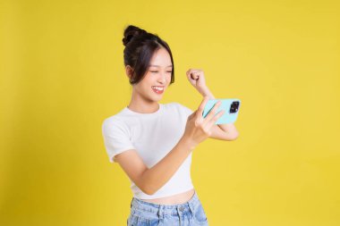 Sarı arka planda telefon oyunu oynayan Asyalı güzel bir kızın portresi.
