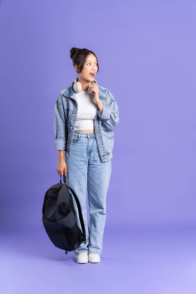 Portrait of a beautiful Asian schoolgirl wearing a backpack on a purple background