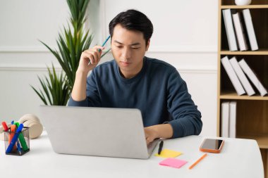 Asyalı bir adamın evde oturup çalışırken görüntüsü