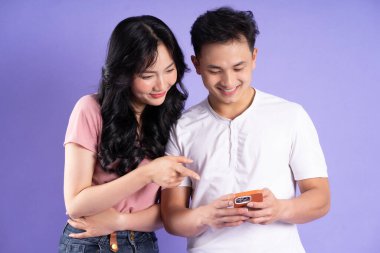 Asyalı bir çiftin elinde akıllı telefon resmi, mor arka planda izole edilmiş.