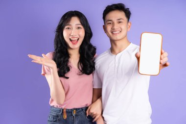 Asyalı bir çiftin elinde akıllı telefon resmi, mor arka planda izole edilmiş.