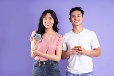 Asyalı bir çiftin elinde akıllı telefon resmi, mor arka planda izole edilmiş.