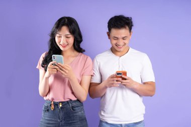 Asyalı bir çiftin elinde akıllı telefon resmi, mor arka planda izole edilmiş.