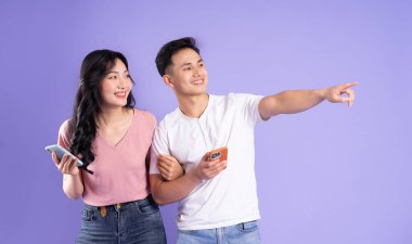 Asyalı bir çiftin elinde akıllı telefon resmi, mor arka planda izole edilmiş.