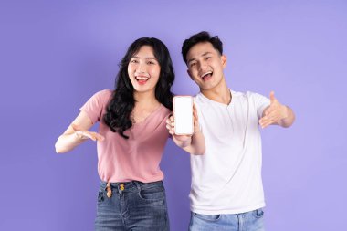 Asyalı bir çiftin elinde akıllı telefon resmi, mor arka planda izole edilmiş.