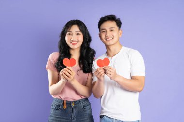 Asyalı bir çiftin elinde kalp çıkartması tutarken görüntüsü, mor arka planda izole edilmiş.
