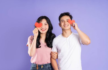 Asyalı bir çiftin elinde kalp çıkartması tutarken görüntüsü, mor arka planda izole edilmiş.