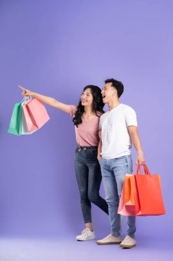 Mor arka planda alışveriş torbaları tutan Asyalı bir çift resmi