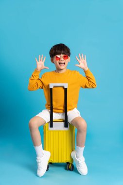 Asyalı çocuk mavi arka planda bavulu çekiyor