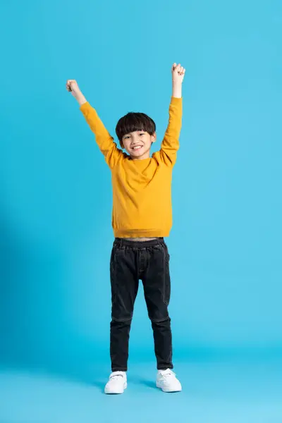 Mavi arka planda poz veren Asyalı çocuğun tüm vücudu.