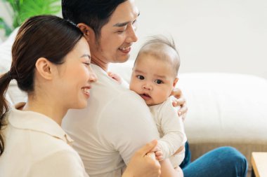 Gülümseyen anne ve baba yeni doğan oğlunu kucağında tutuyor.