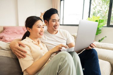 Asyalı bir çiftin evdeki koltukta oturduğu görüntüsü.