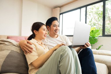 Asyalı bir çiftin evdeki koltukta oturduğu görüntüsü.