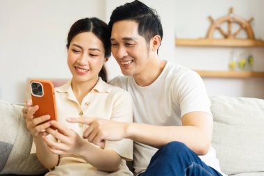 Asyalı bir çiftin evdeki koltukta oturduğu görüntüsü.