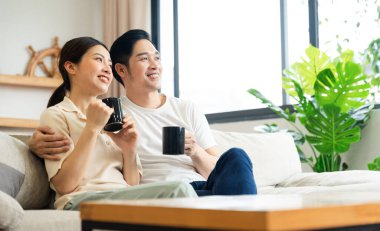 Asyalı bir çiftin evdeki koltukta oturduğu görüntüsü.