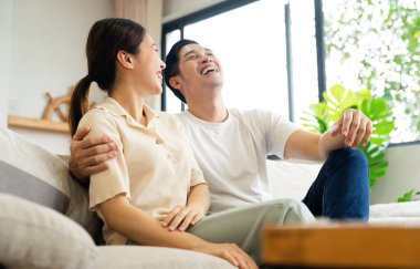 Asyalı bir çiftin evdeki koltukta oturduğu görüntüsü.