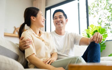 Asyalı bir çiftin evdeki koltukta oturduğu görüntüsü.