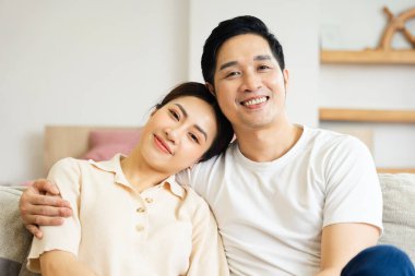 Asyalı bir çiftin evdeki koltukta oturduğu görüntüsü.