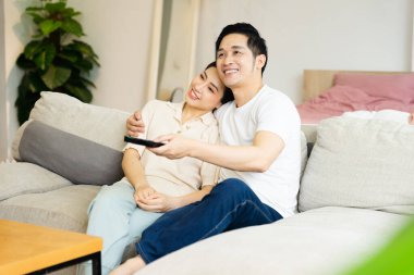 Asyalı bir çiftin evdeki koltukta oturduğu görüntüsü.