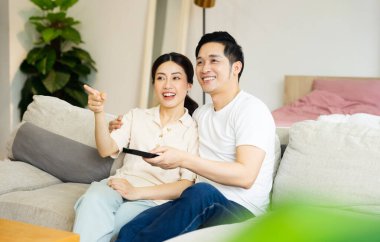 Asyalı bir çiftin evdeki koltukta oturduğu görüntüsü.