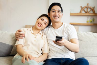 Asyalı bir çiftin evdeki koltukta oturduğu görüntüsü.