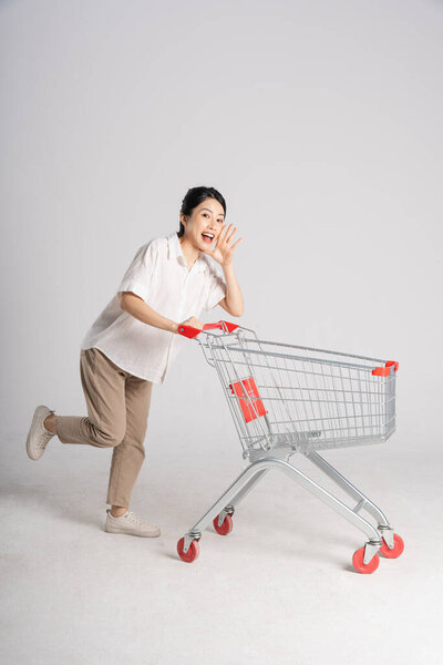 Smiling woman happily pushing a supermarket cart, isolated on white background
