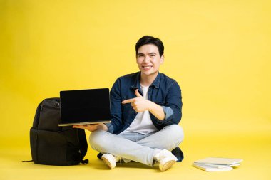 Sarı arka planda poz veren Asyalı erkek öğrencinin portresi